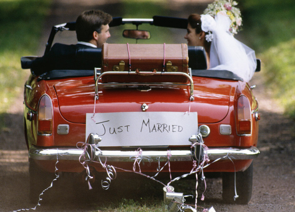 A vintage red convertible featuring a "Just Married" sign and decorative tins attached to the bumper