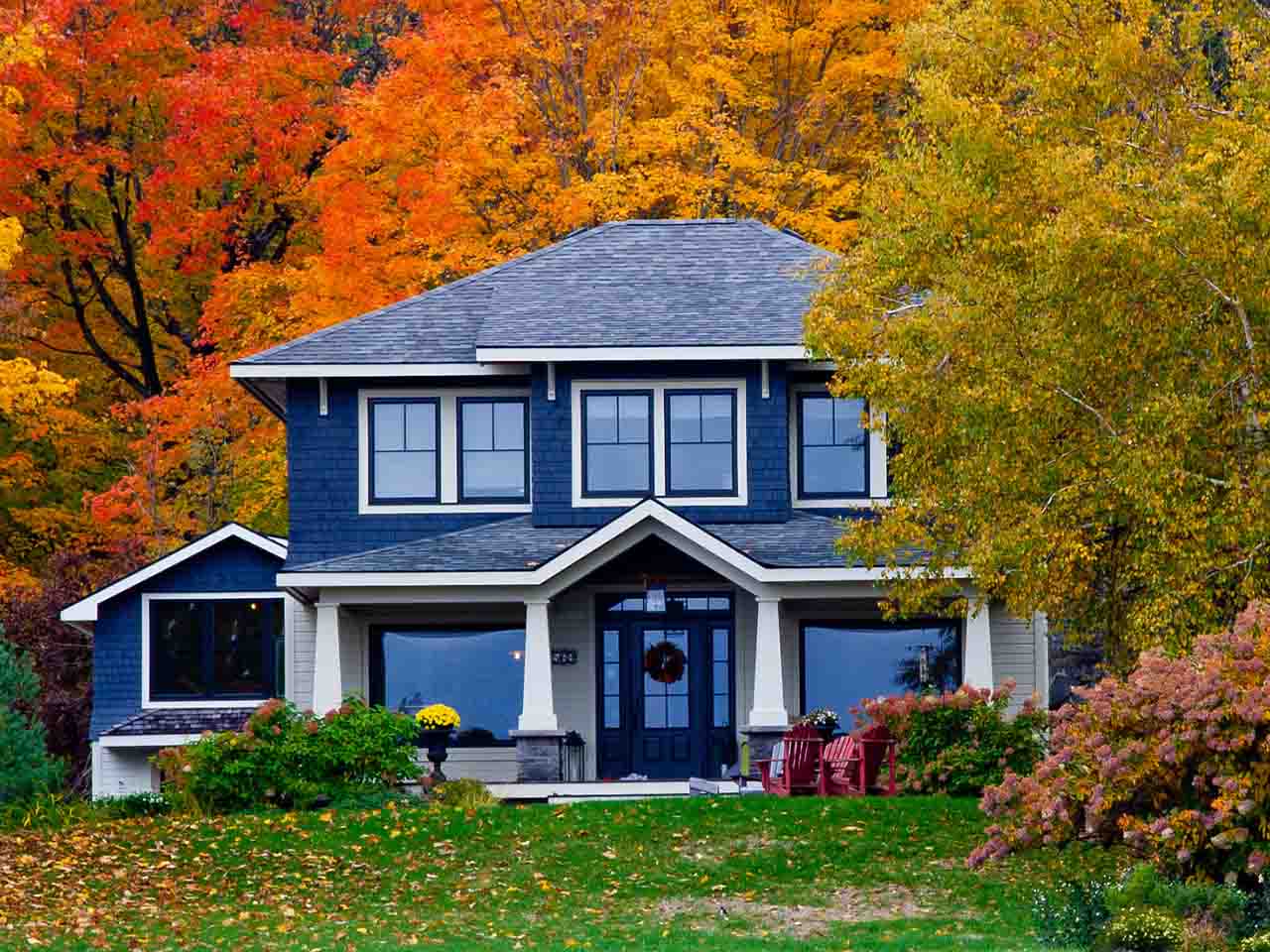 A blue-and-white two-story house surrounded by vibrant red, orange, and yellow autumn trees.